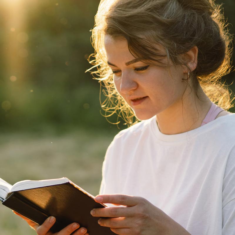 Young woman reading her Bible outside on a sunny day - Carolina Counseling, Greenville, NC offering Christian Counseling