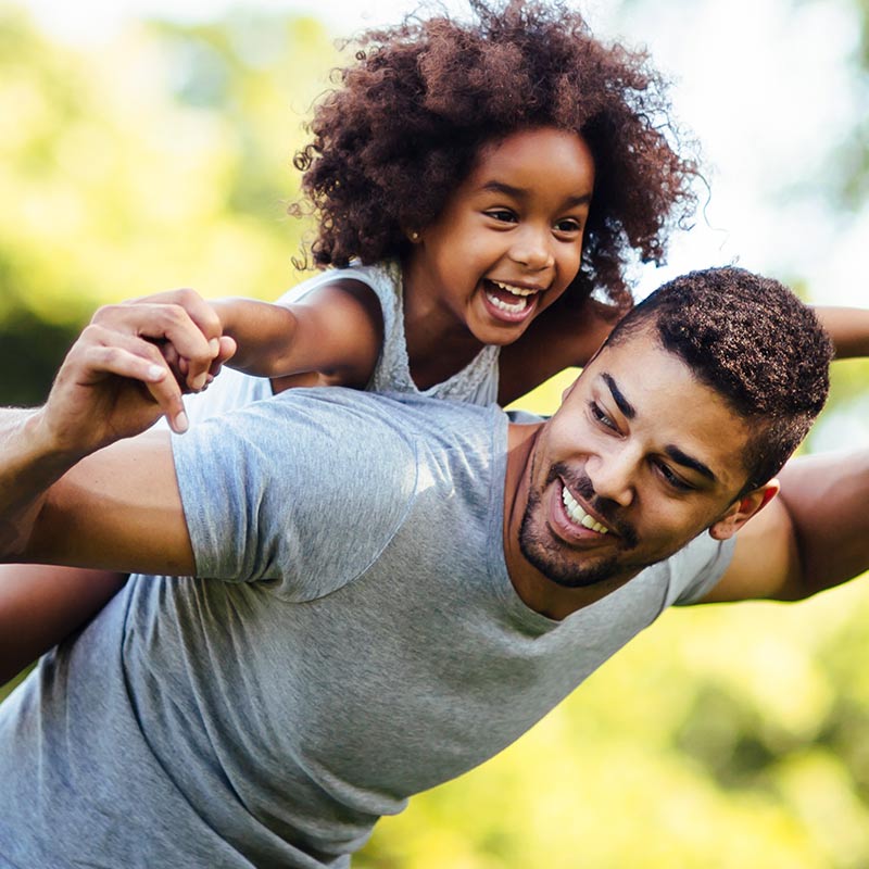 Smiling Father giving Young Daughter a ride on his back, outside - Triple P Postive Parenting with Carolina Counseling, Greenville, NC